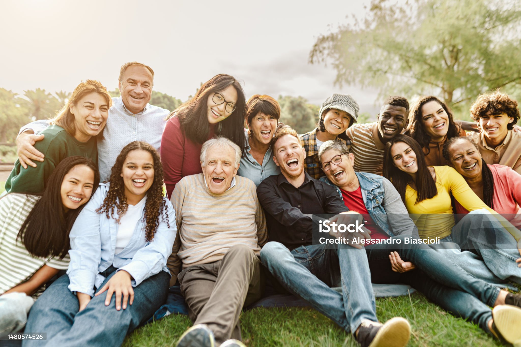 Happy multigenerational people having fun sitting on grass in a public park